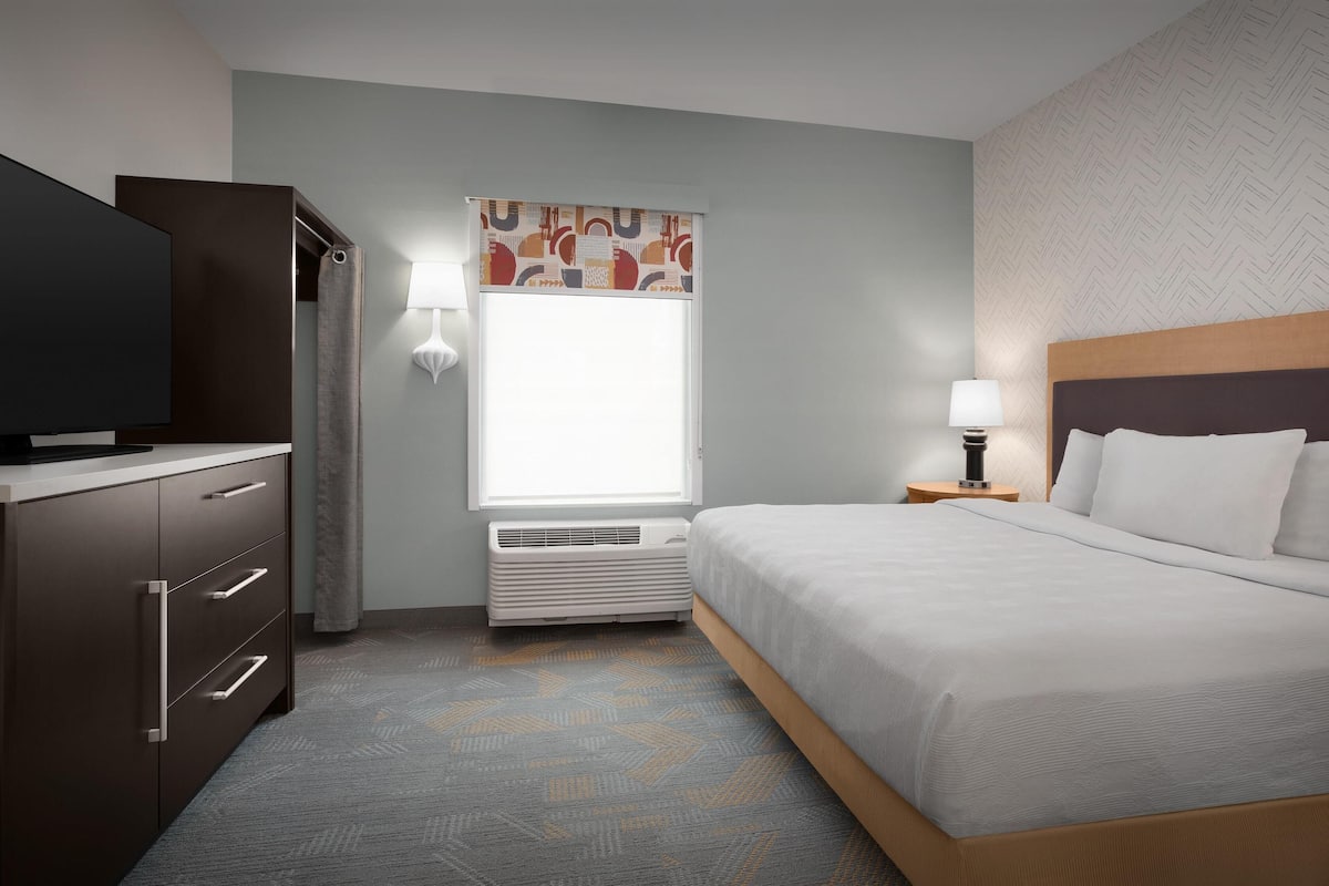 A hotel room with a bed, a TV, a desk, a lamp, and a window with curtains.
