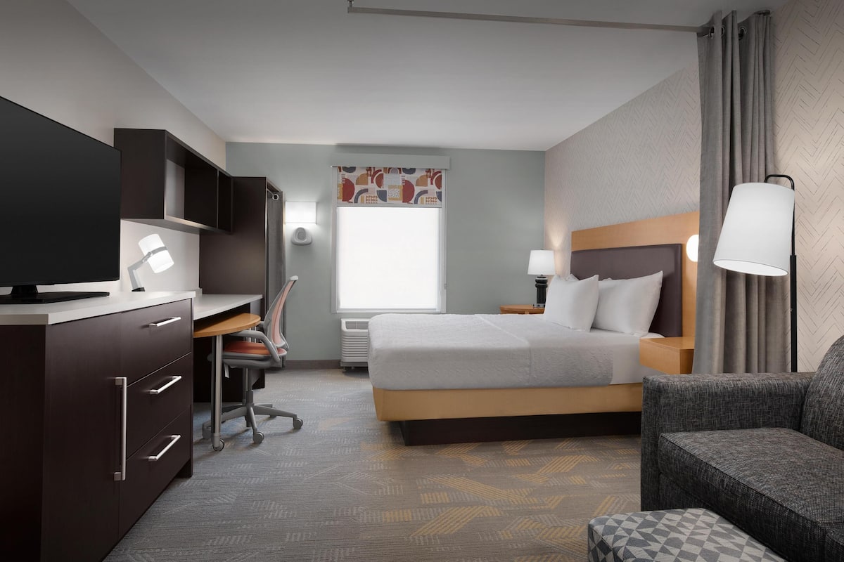 A hotel room with a bed, a desk, a chair, a TV, and a lamp.