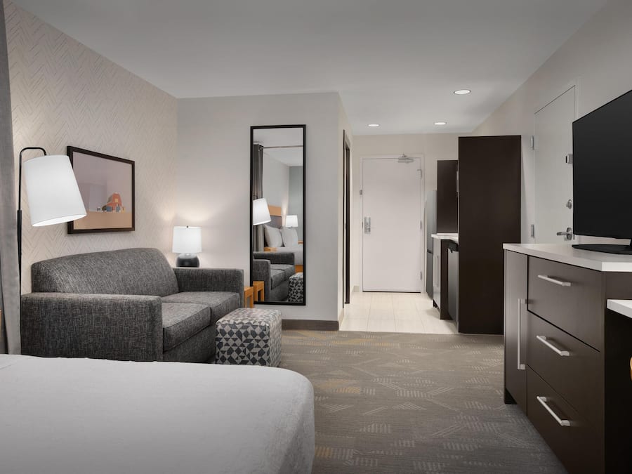 Een moderne hotelkamer met een bed, een bank, een klein tafeltje, een televisie en een badkamer die door een geopende deur zichtbaar is.