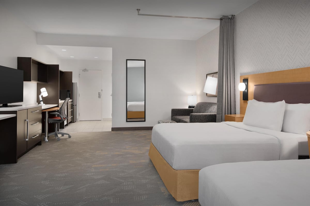 A hotel room with two beds, a desk with a computer, a chair, a TV, and a large mirror.