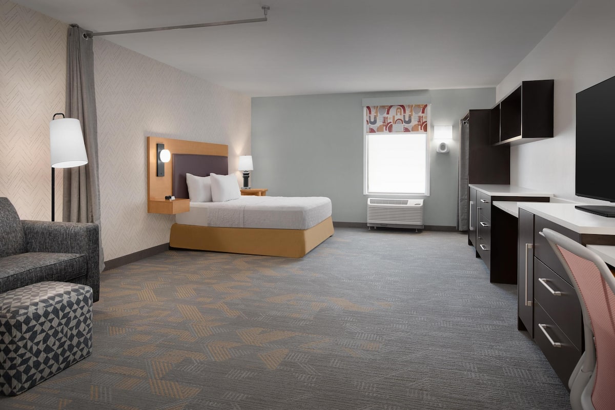 A hotel room with a bed, a desk, a chair, a lamp, a TV, and a window with curtains.