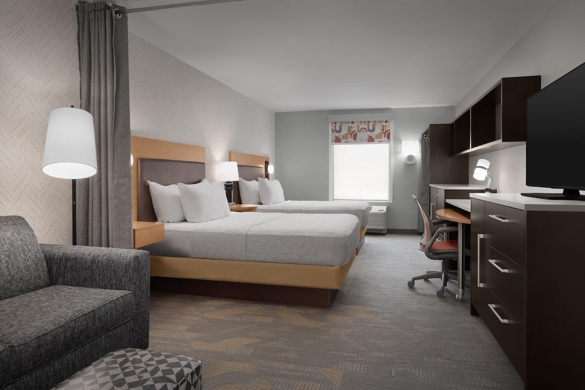 A hotel room with two beds, a desk, a chair, and a TV.