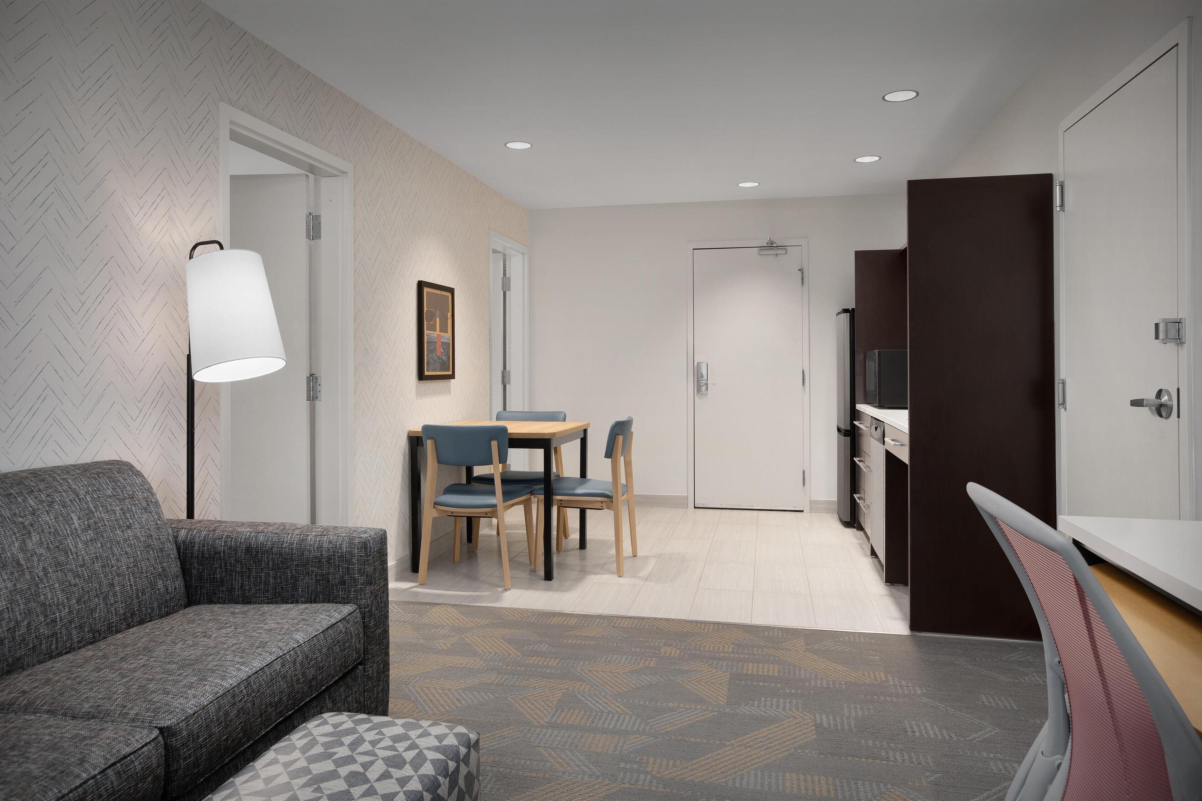 Ein modernes Hotelzimmer mit einer Couch, einem Esstisch mit Stühlen, einer Küchenzeile und einem großen Spiegel.