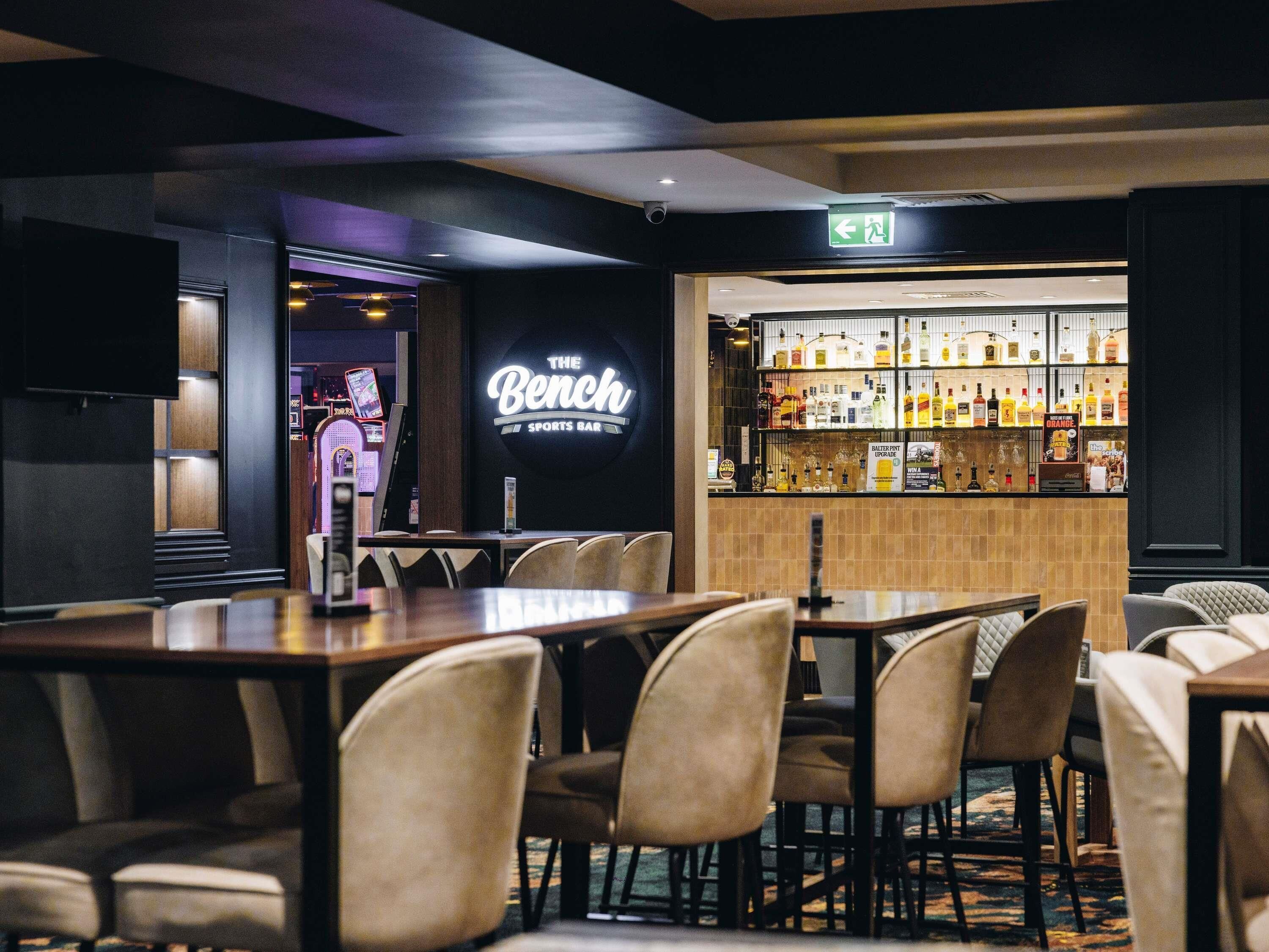 Eine Bar mit einer Neonreklame, einer Spirituosenpräsentation und Sitzmöglichkeiten.