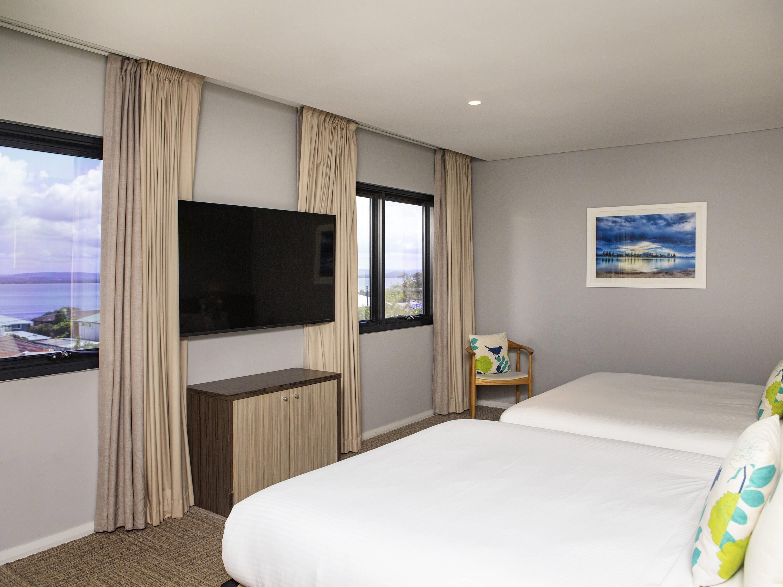 Una habitación de hotel con cama, televisión, escritorio, silla y ventana con cortinas.