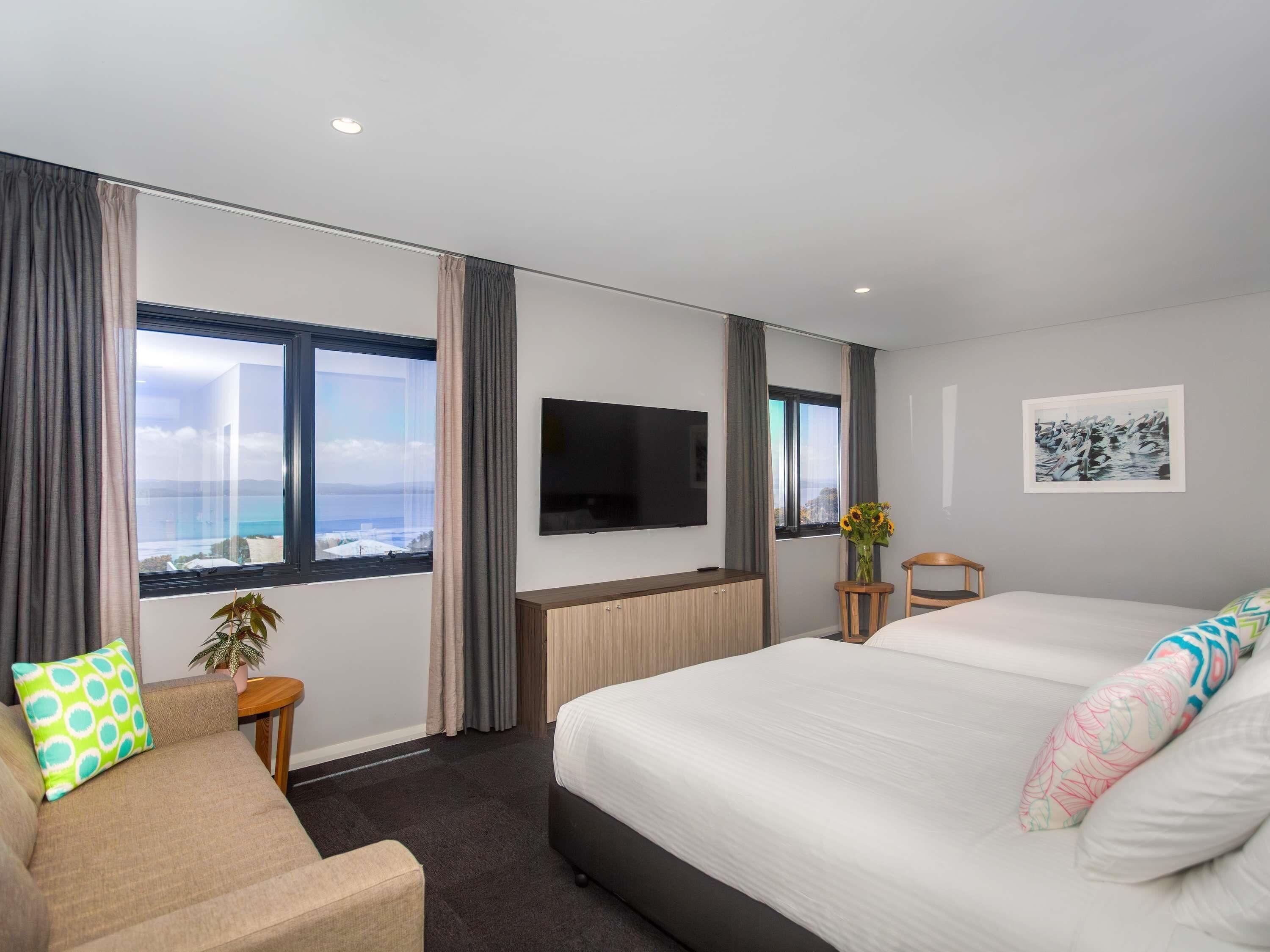 A hotel room with a large bed, a sofa, a TV, and a window with curtains.