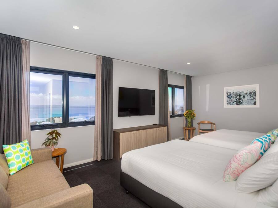 A hotel room with a large bed, a sofa, a TV, and a window with curtains.