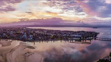A coastal cityscape with a prominent bridge connecting two land masses, a sandy beach area, and a calm body of water reflecting the city lights.