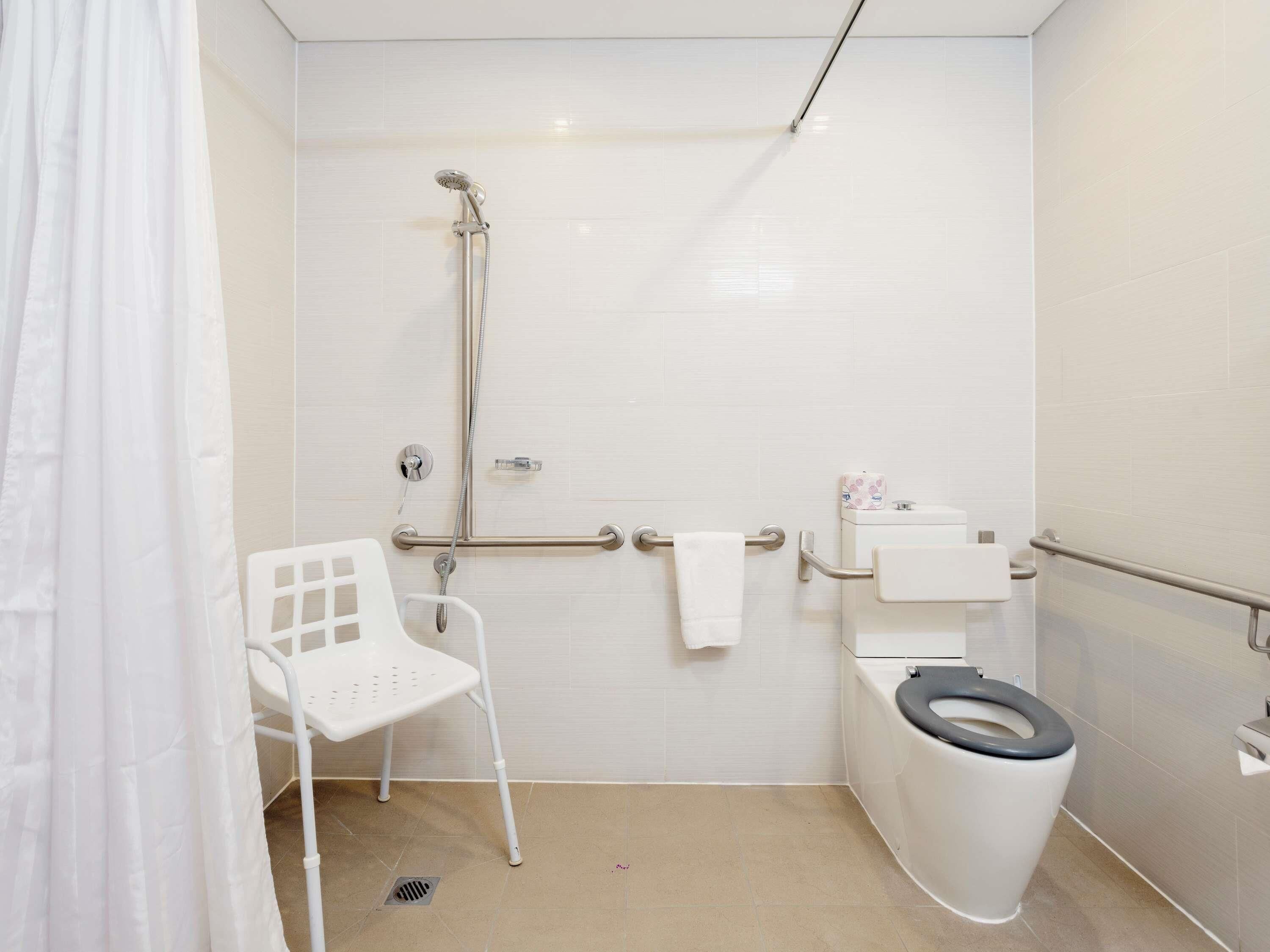 Un baño con ducha, inodoro y una silla blanca.