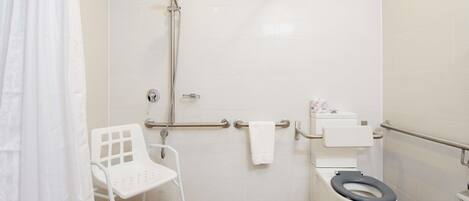 Un baño con ducha, inodoro y una silla blanca.