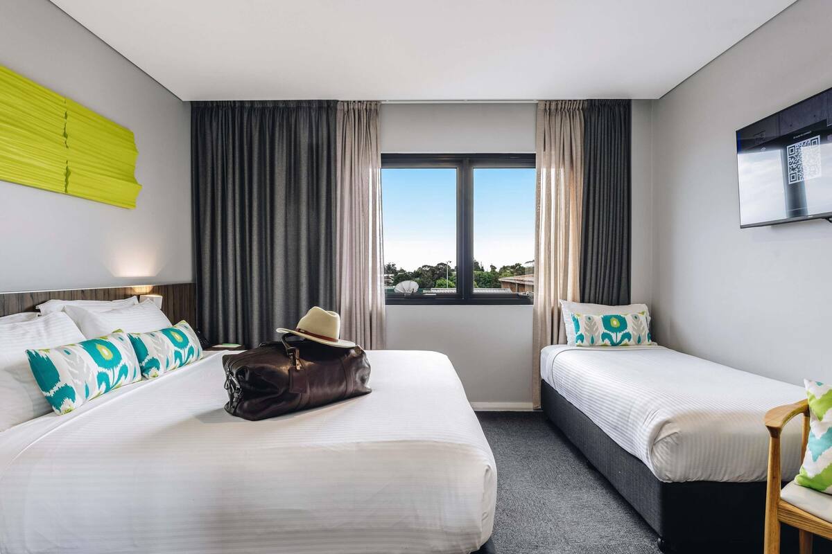 Habitación de hotel con dos camas, un ventanal grande y vistas al exterior.