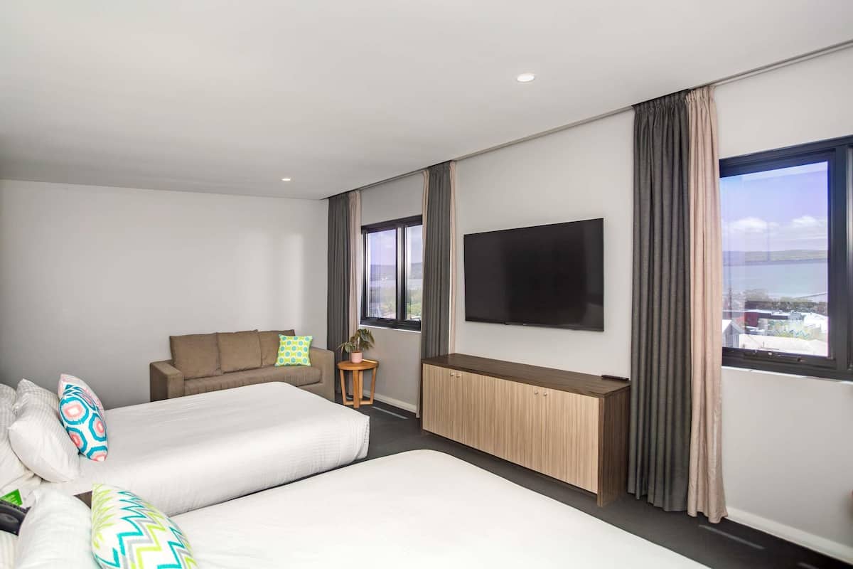 Habitación de hotel con dos camas, un sofá, un televisor y vista al mar.