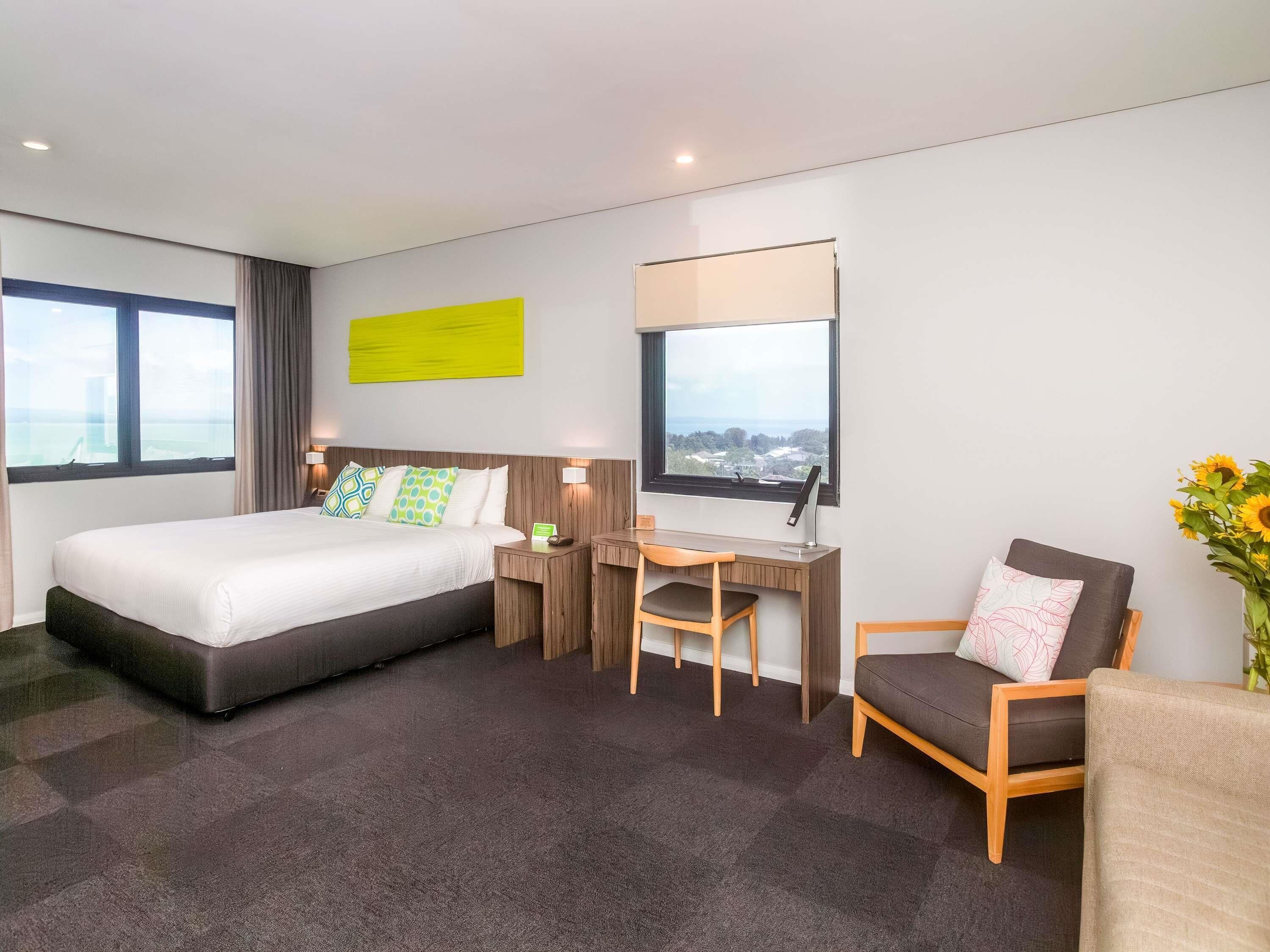 Une chambre d’hôtel équipée d’un lit, d’un bureau, d’une chaise et offrant une vue sur la ville par la fenêtre.