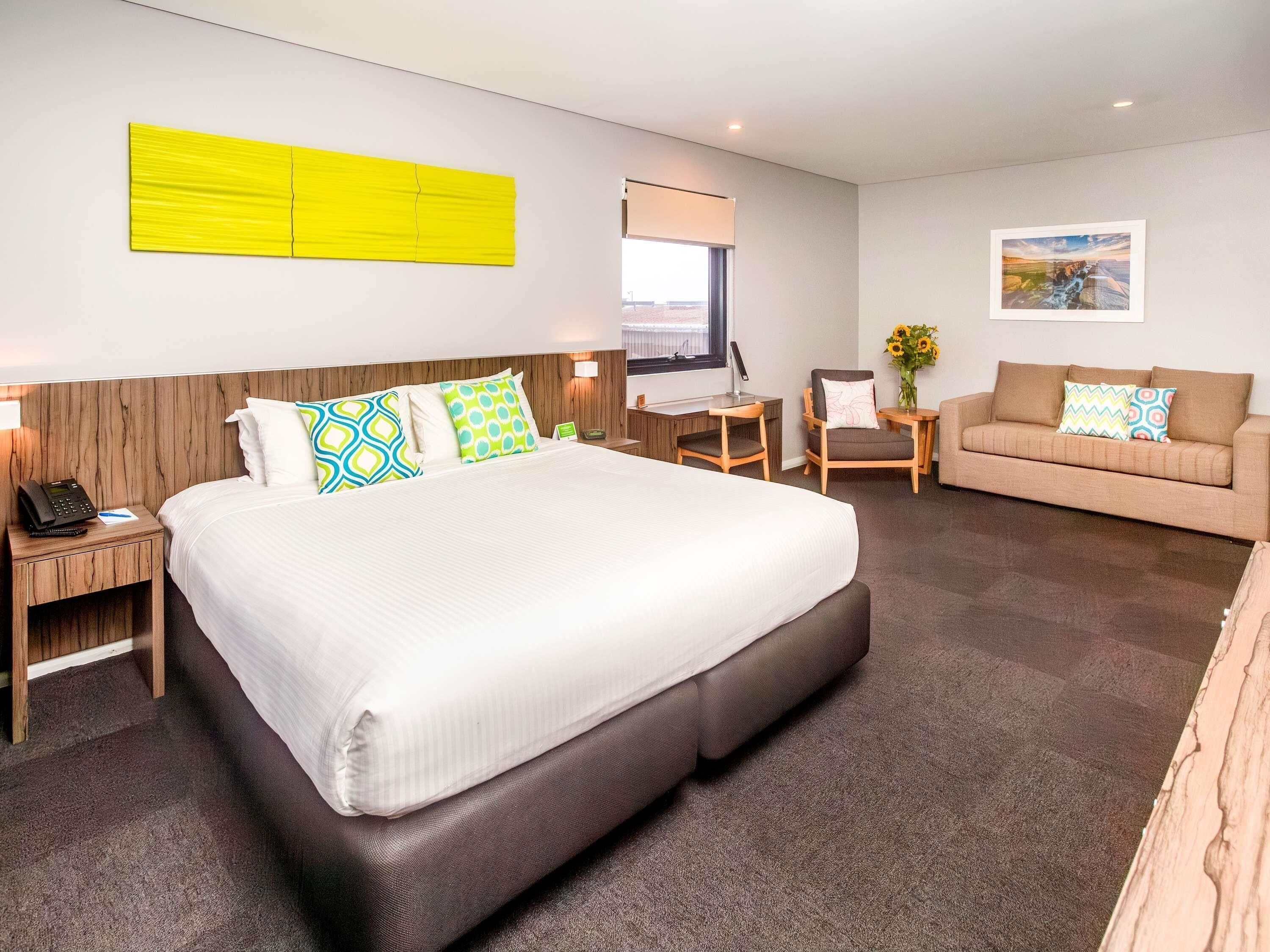 Habitació d'hotel amb un llit gran, un sofà, una taula de treball i un quadre a la paret.