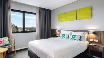 Habitación de hotel con una cama grande, un escritorio con silla, una ventana con cortinas y un aplique de pared.