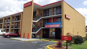Un motel de dos pisos con fachada roja y color crema, un estacionamiento visible y un letrero que dice 'EconoLodge'.