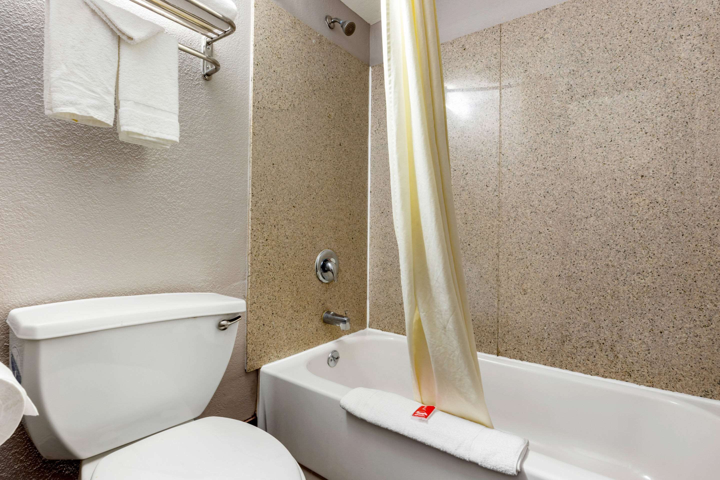 Une salle de bain comprenant des toilettes, une baignoire avec un rideau de douche et un porte-serviettes avec deux serviettes.