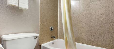 A bathroom with a toilet, a bathtub with a shower curtain, and a towel rack with two towels.