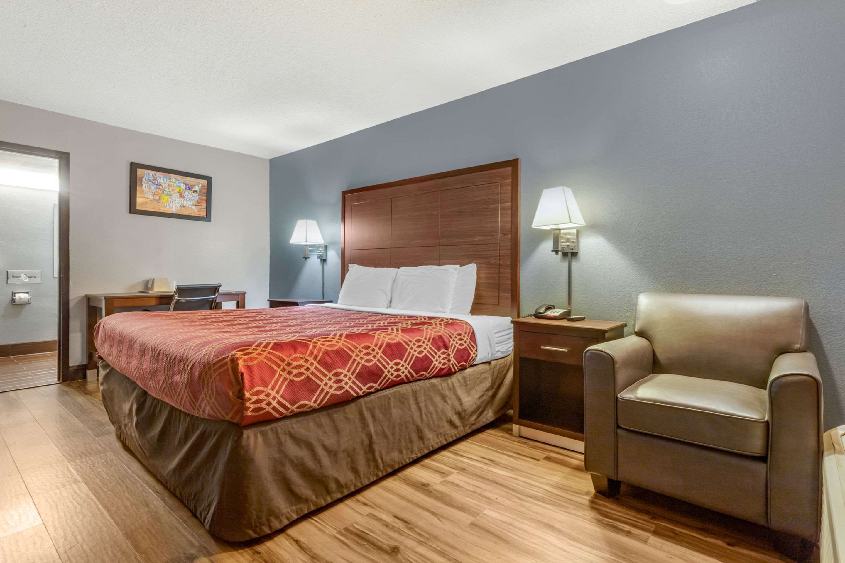 Una habitación de hotel con cama, escritorio, silla y mesita de noche.