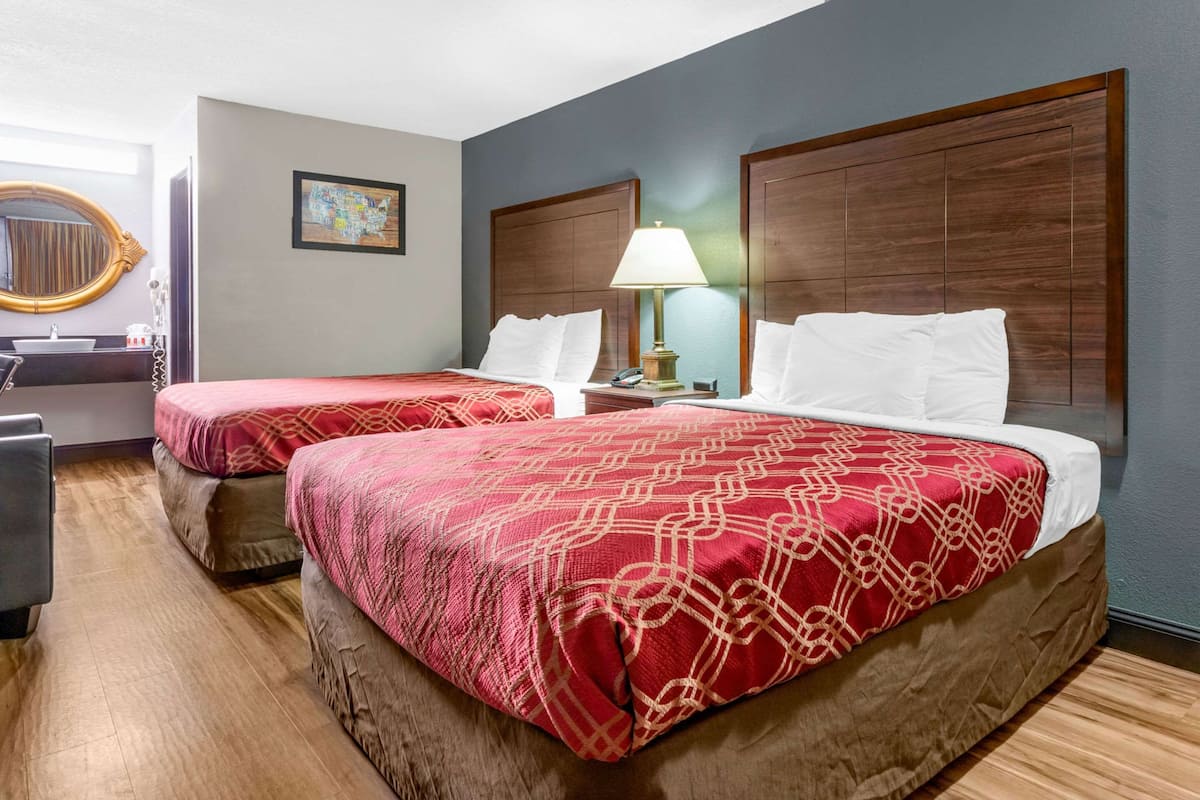 A hotel room with two beds, a bedside table with a lamp, a mirror, and a painting on the wall.