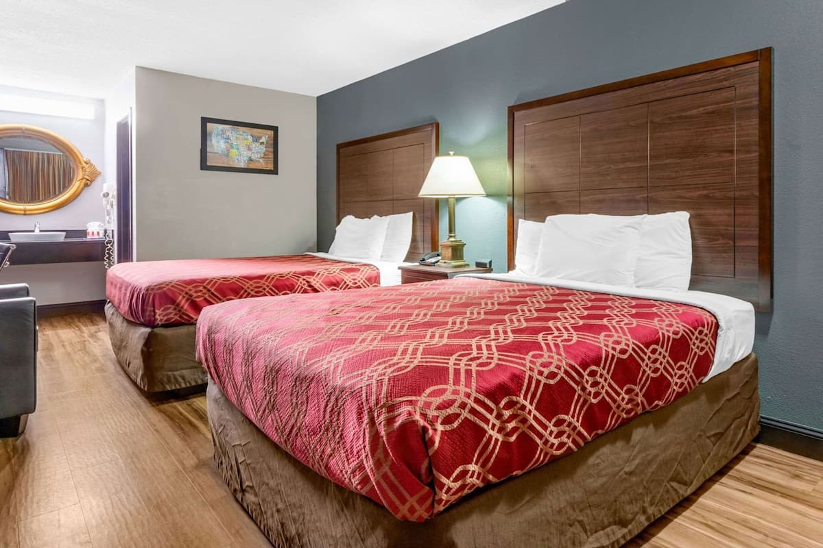 A hotel room with two beds, a desk, a lamp, and a map on the wall.