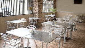 Un restaurante con mesas y sillas de metal, un muro de piedra y vistas a través de rejas.
