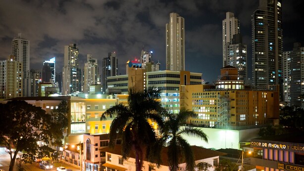 Un paisaje urbano nocturno con edificios altos, palmeras y calles iluminadas.