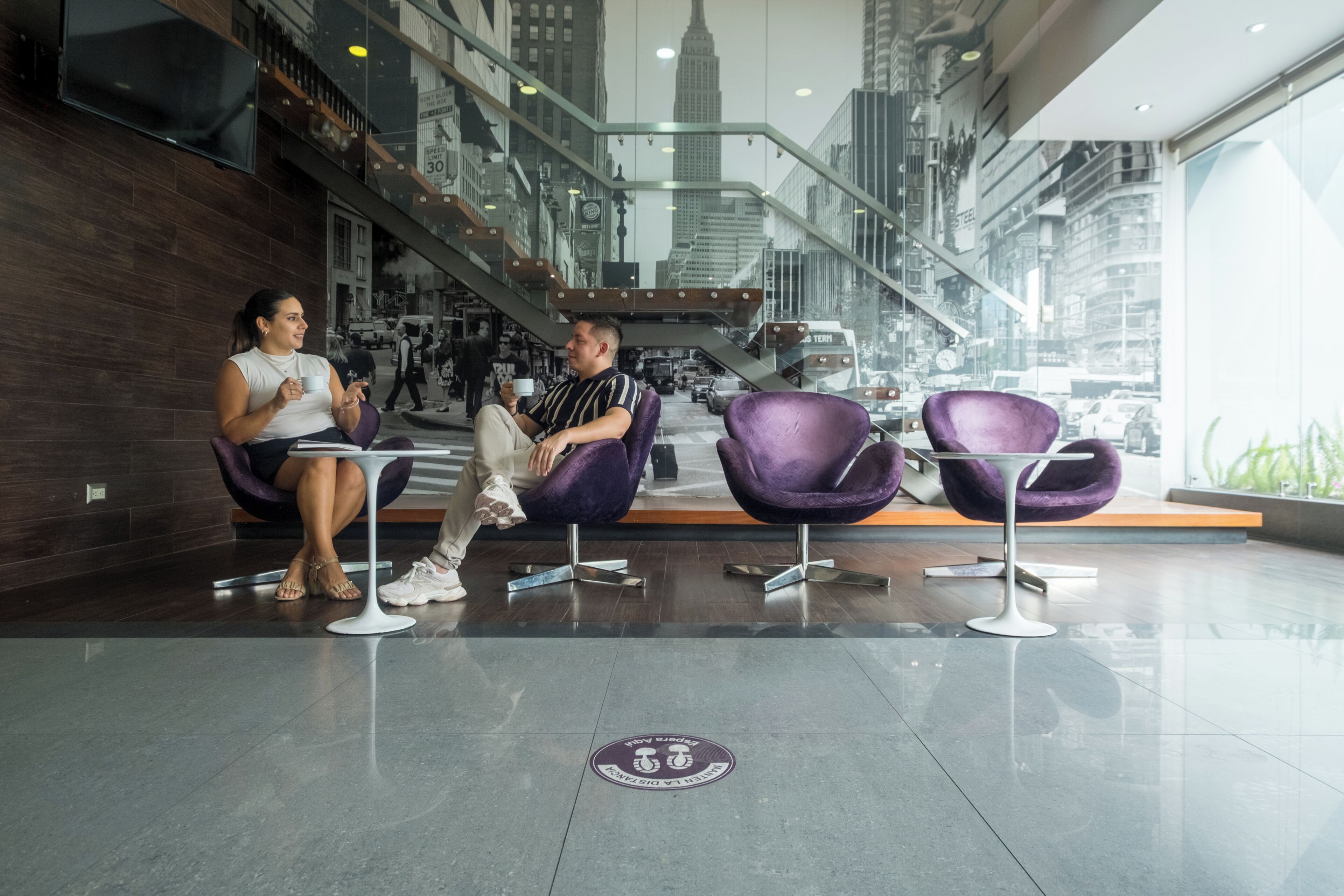 A modern interior with a seating area featuring purple chairs and a glass railing overlooking a cityscape.