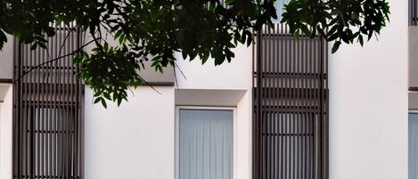 Un edificio moderno con varios balcones, ventanas amplias y un árbol en primer plano.
