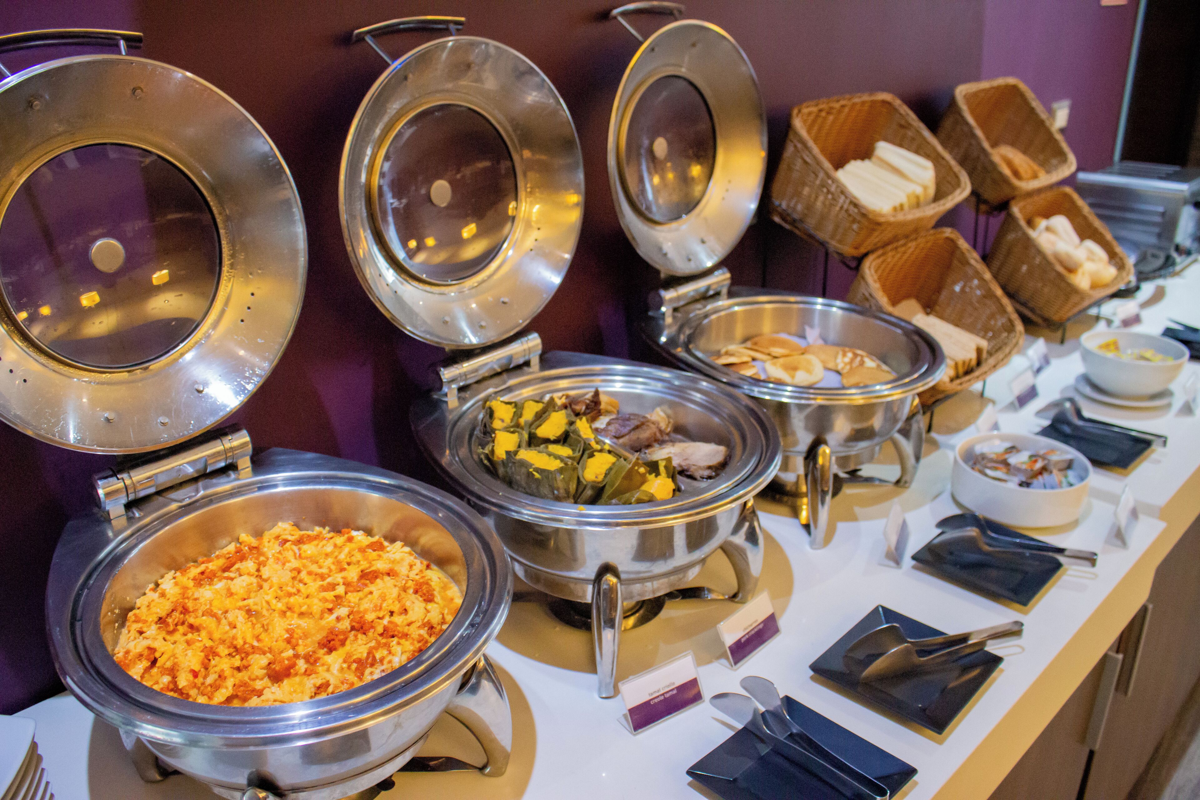 A buffet with various food items in metal serving dishes, arranged on a table with utensils and napkins.