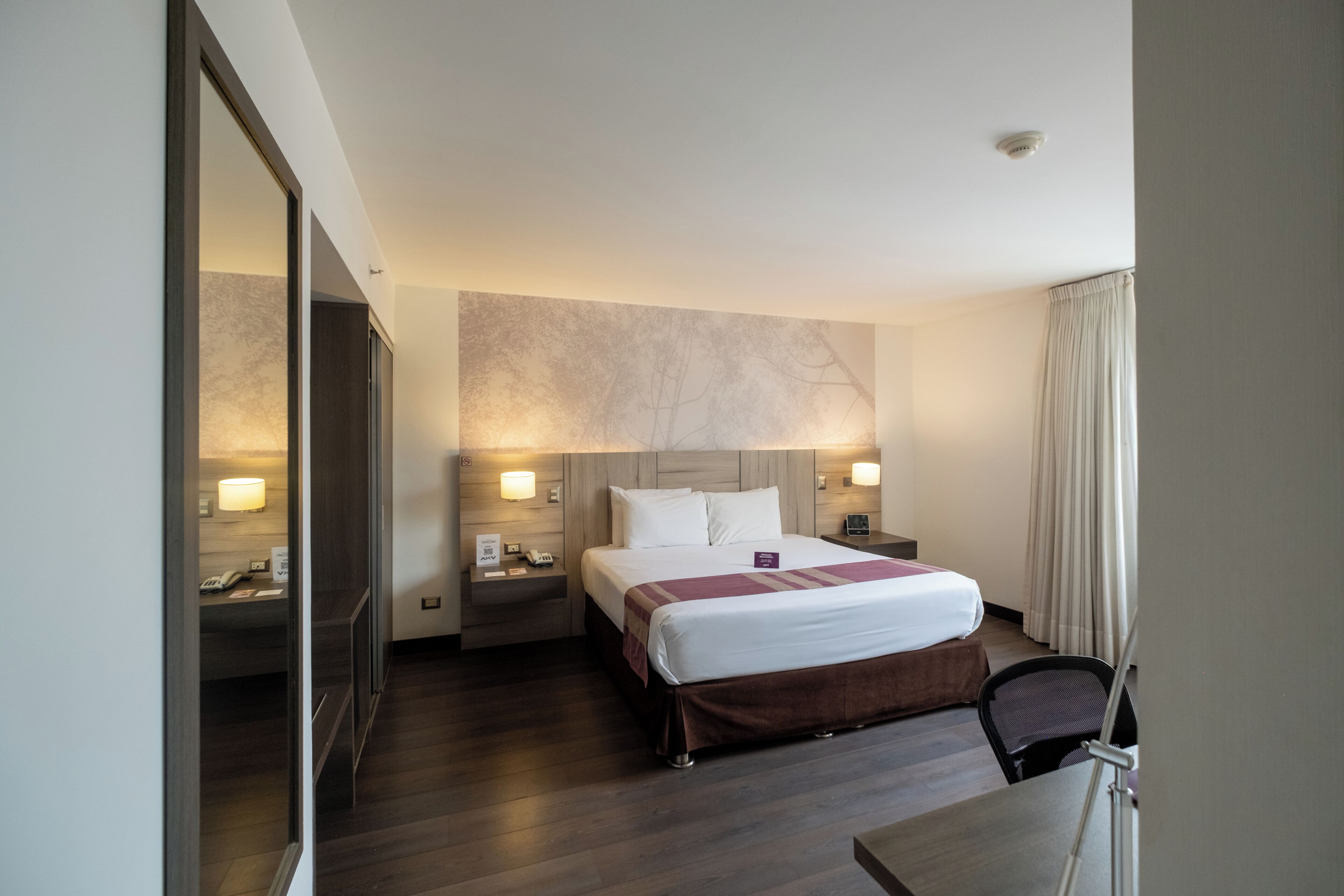 Una habitación de hotel con una cama grande, mesitas de noche, un escritorio y una silla.