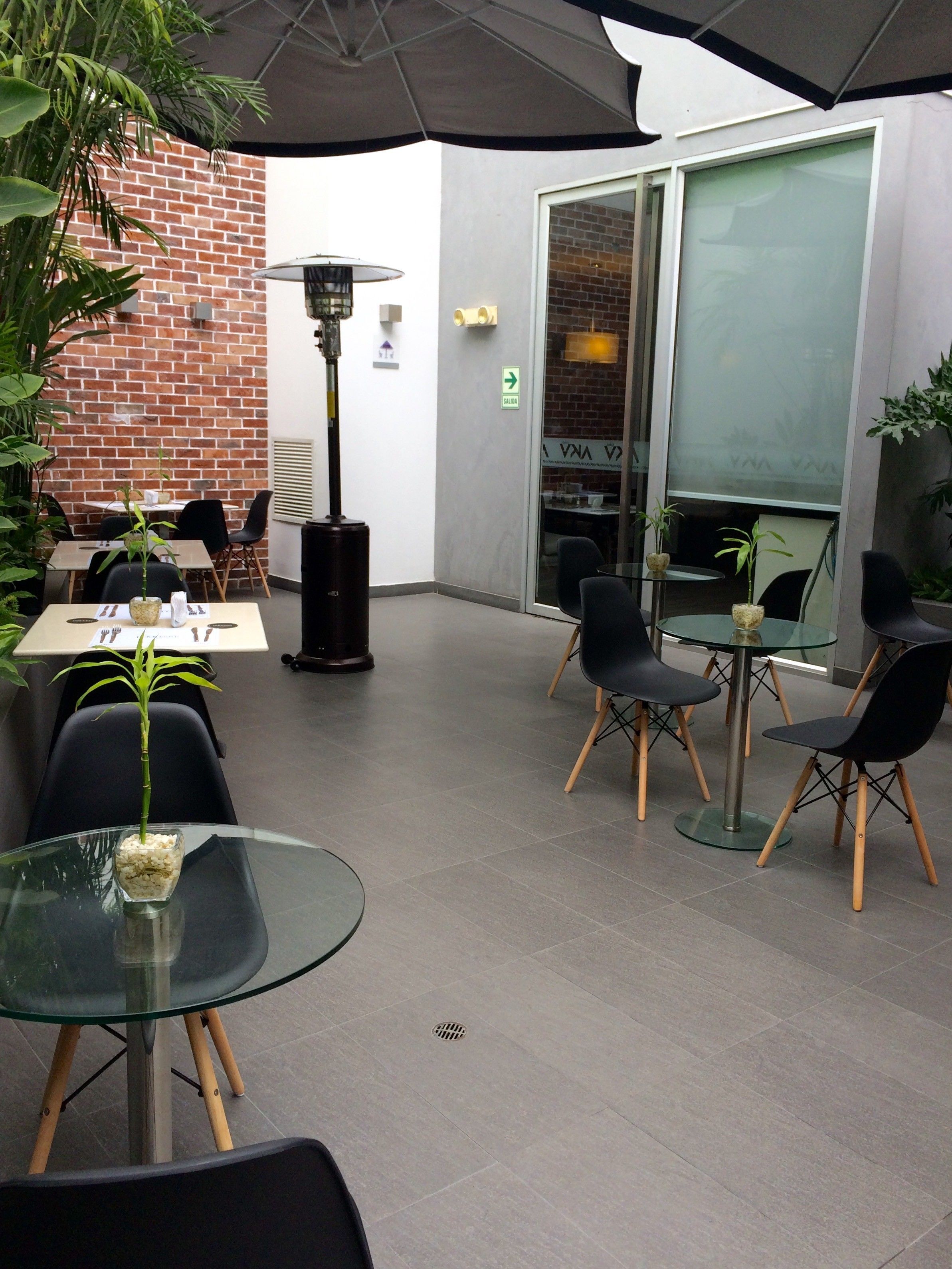 An outdoor seating area with tables and chairs, a glass partition, and a brick wall.