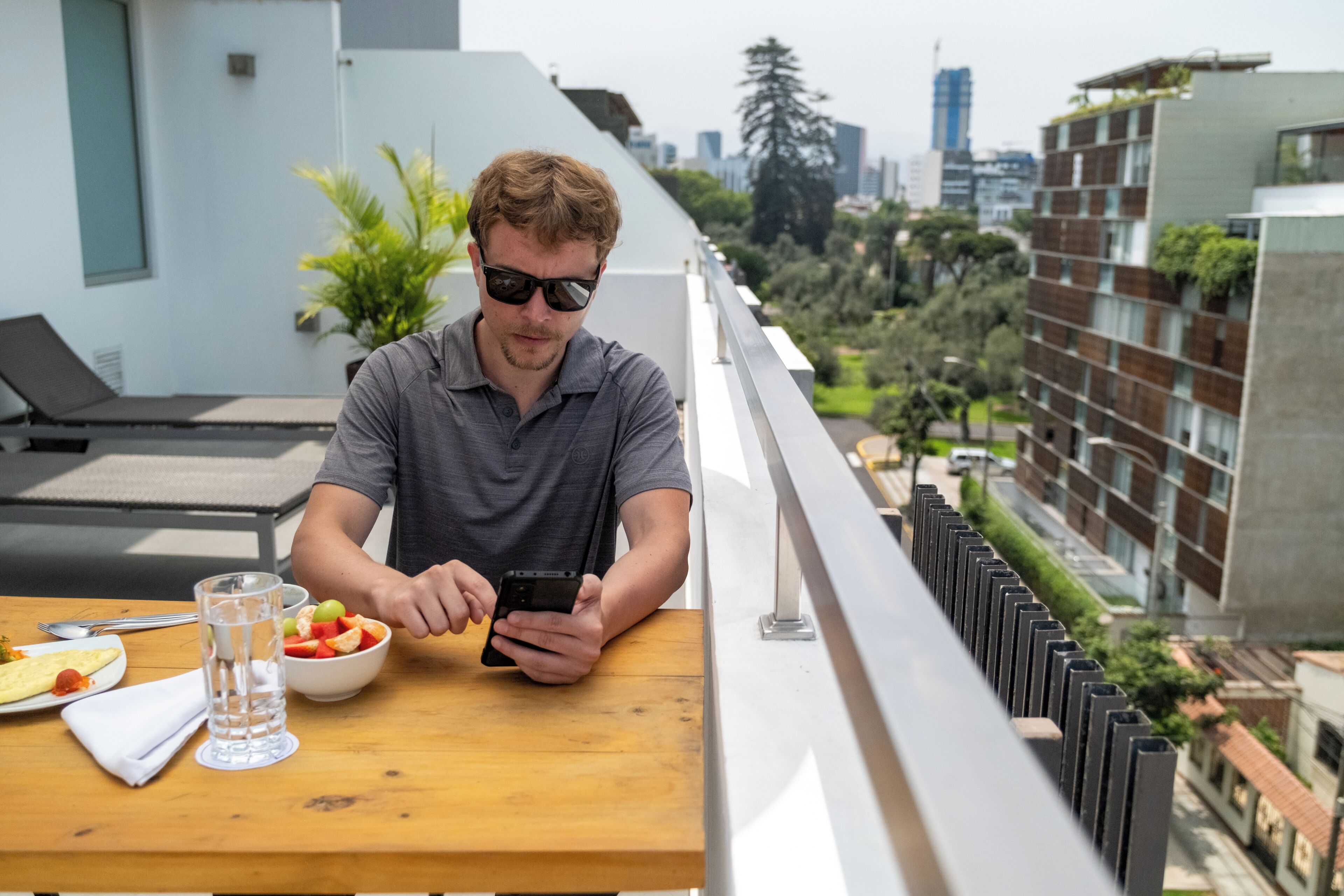 Um homem sentado à mesa com uma tigela de frutas, um copo de água e um prato de comida.