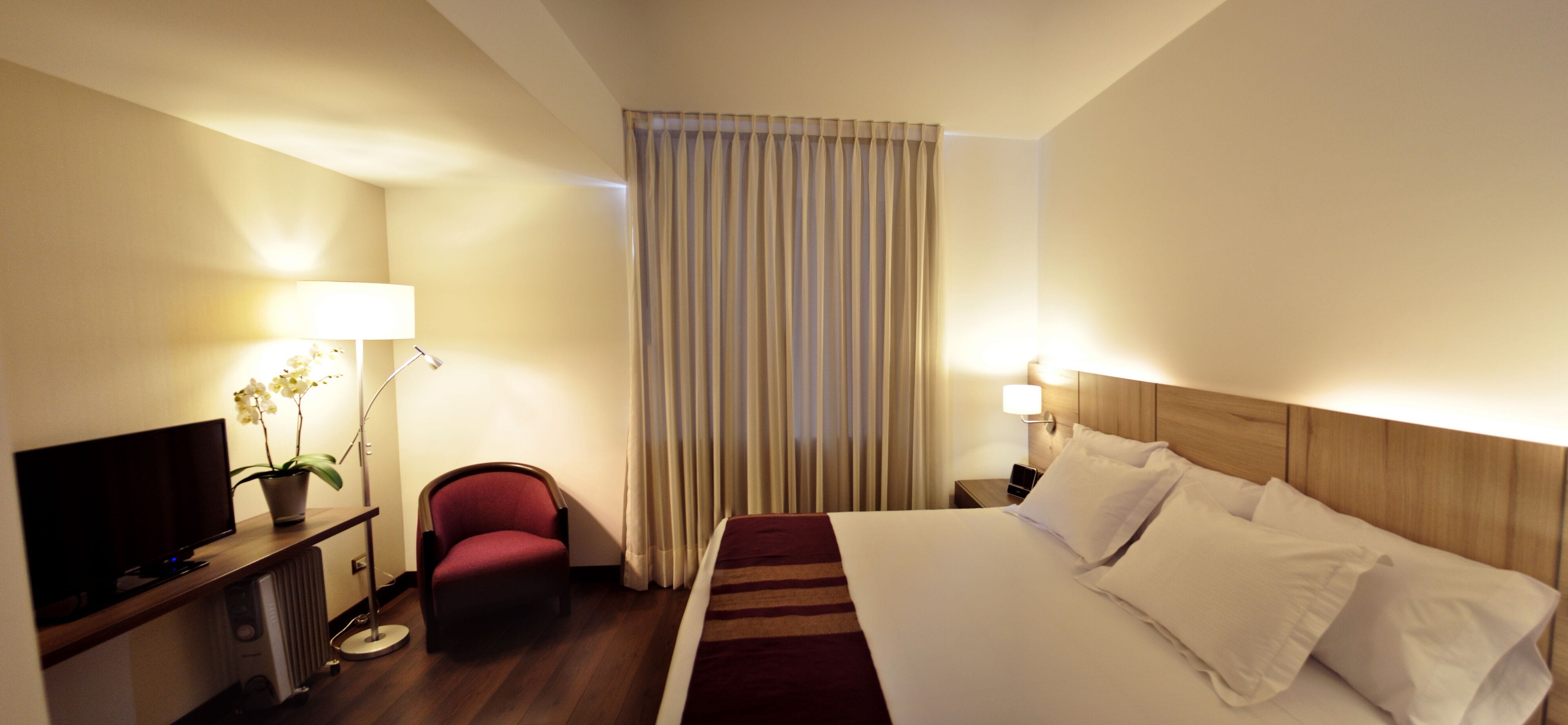 Camera d'albergo con un letto, una TV, una scrivania con un computer, una sedia e una finestra con tende.