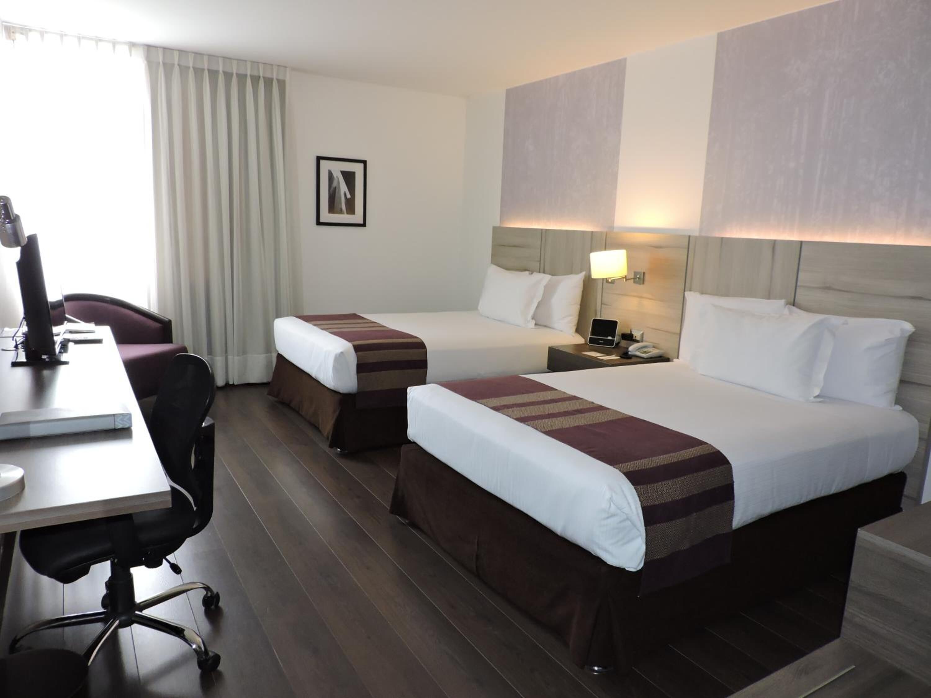 Ein Hotelzimmer mit zwei Betten, einem Schreibtisch mit Computer und einem Stuhl.
