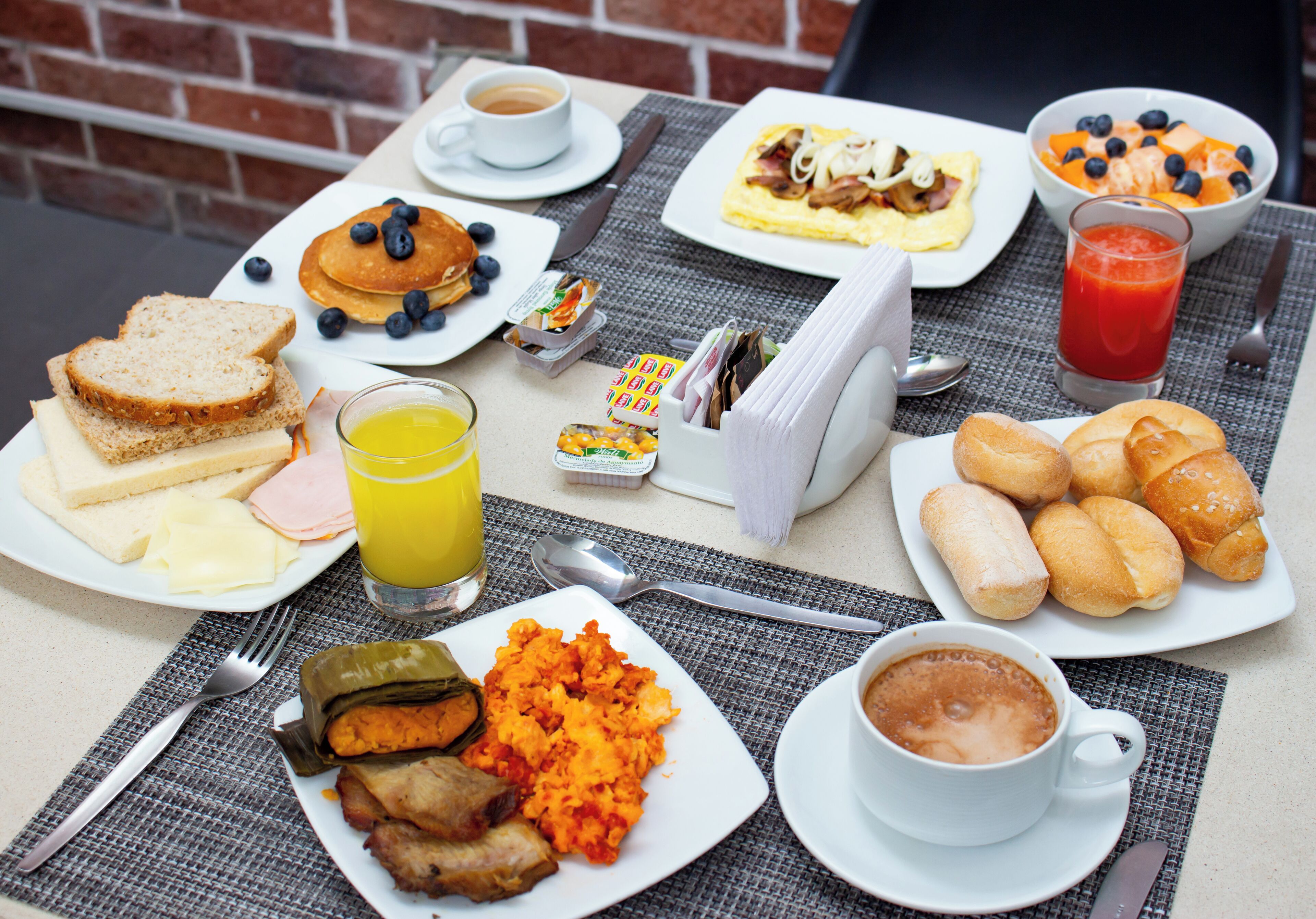A breakfast table with various food items, including pancakes, toast, and a bowl of fruit.
