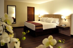 A hotel room with a wooden bed, two bedside lamps, a nightstand, and a mirror on the wall. - Aku Hotels (Lima)