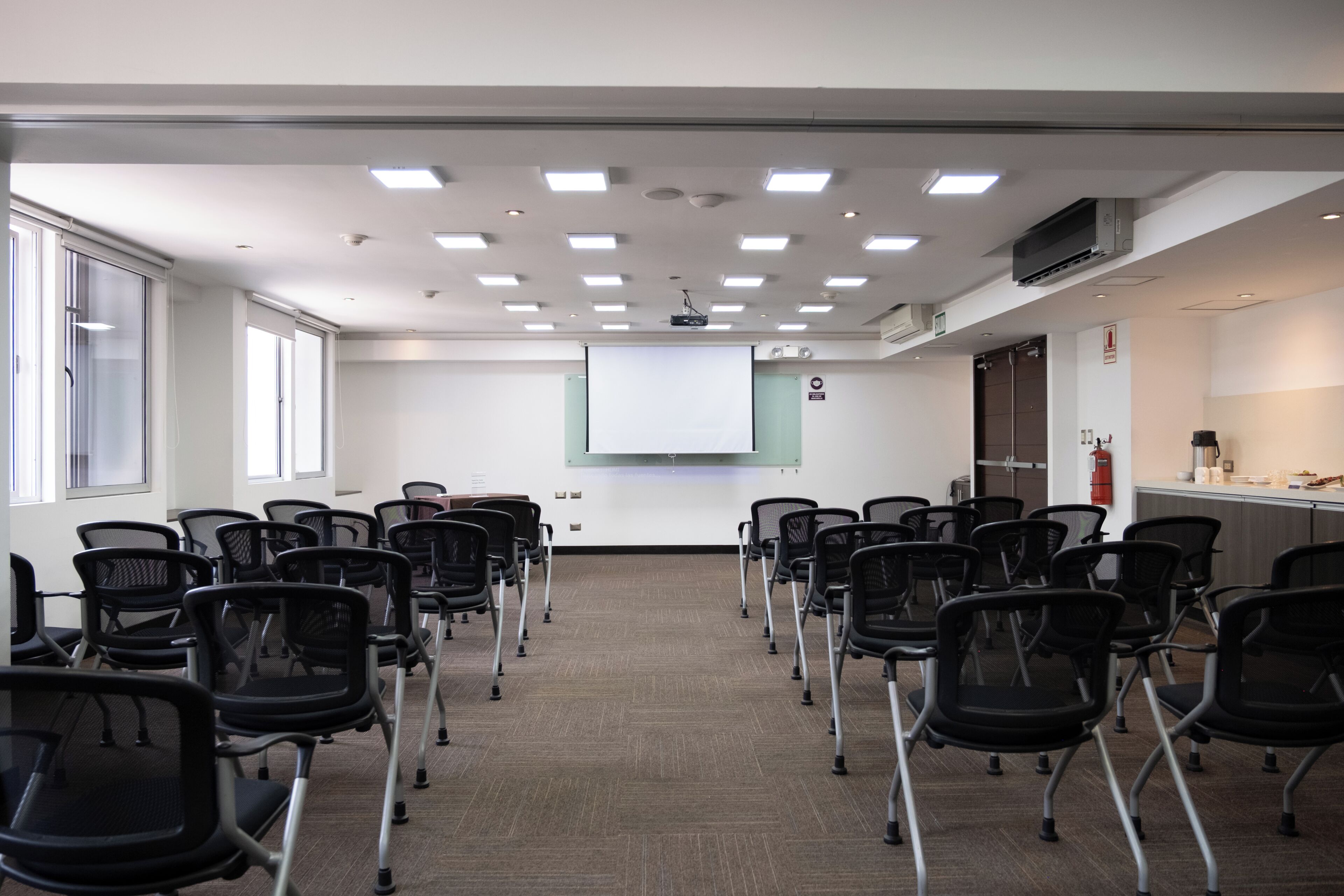 A conference room with rows of chairs, a projector screen, and a whiteboard.