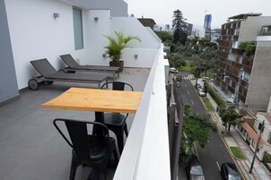 A rooftop terrace with a table and chairs, lounge chairs, and a potted plant.