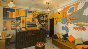 Zona de recepción con un mostrador de madera, un letrero de recepción y una pared con un mapa y coloridas obras de arte.