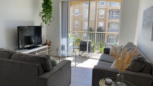 A modern living room with a flat-screen TV, two grey sofas, a glass coffee table, and a balcony with potted plants. - Orlando Select Vacation Homes (Kissimmee)
