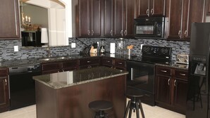 A modern kitchen with dark wood cabinets, a granite countertop, a built-in oven, a microwave, and a refrigerator. - Orlando Select Vacation Homes (Kissimmee)