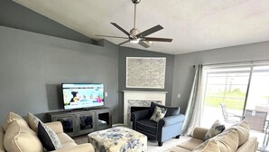 A living room with two beige sofas, a television, a fireplace, and a ceiling fan. - Orlando Select Vacation Homes (Kissimmee)