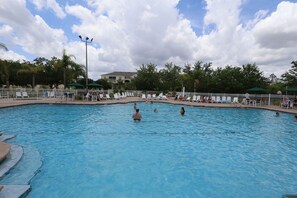 A swimming pool with people in the water and on the deck, surrounded by a white fence and palm trees. - Orlando Select Vacation Homes (Kissimmee)