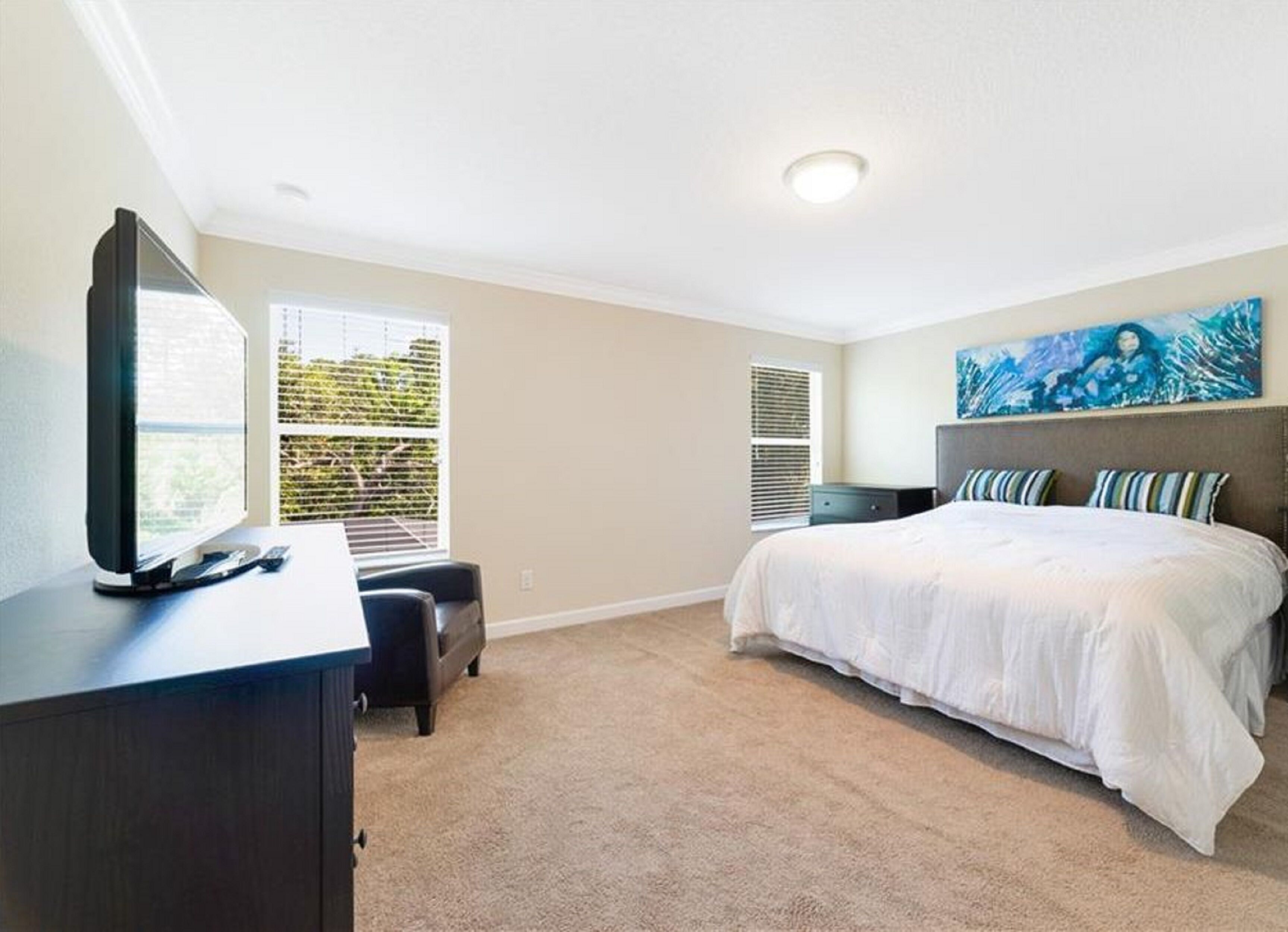 A bedroom with a bed, a desk, a TV, and a painting on the wall.