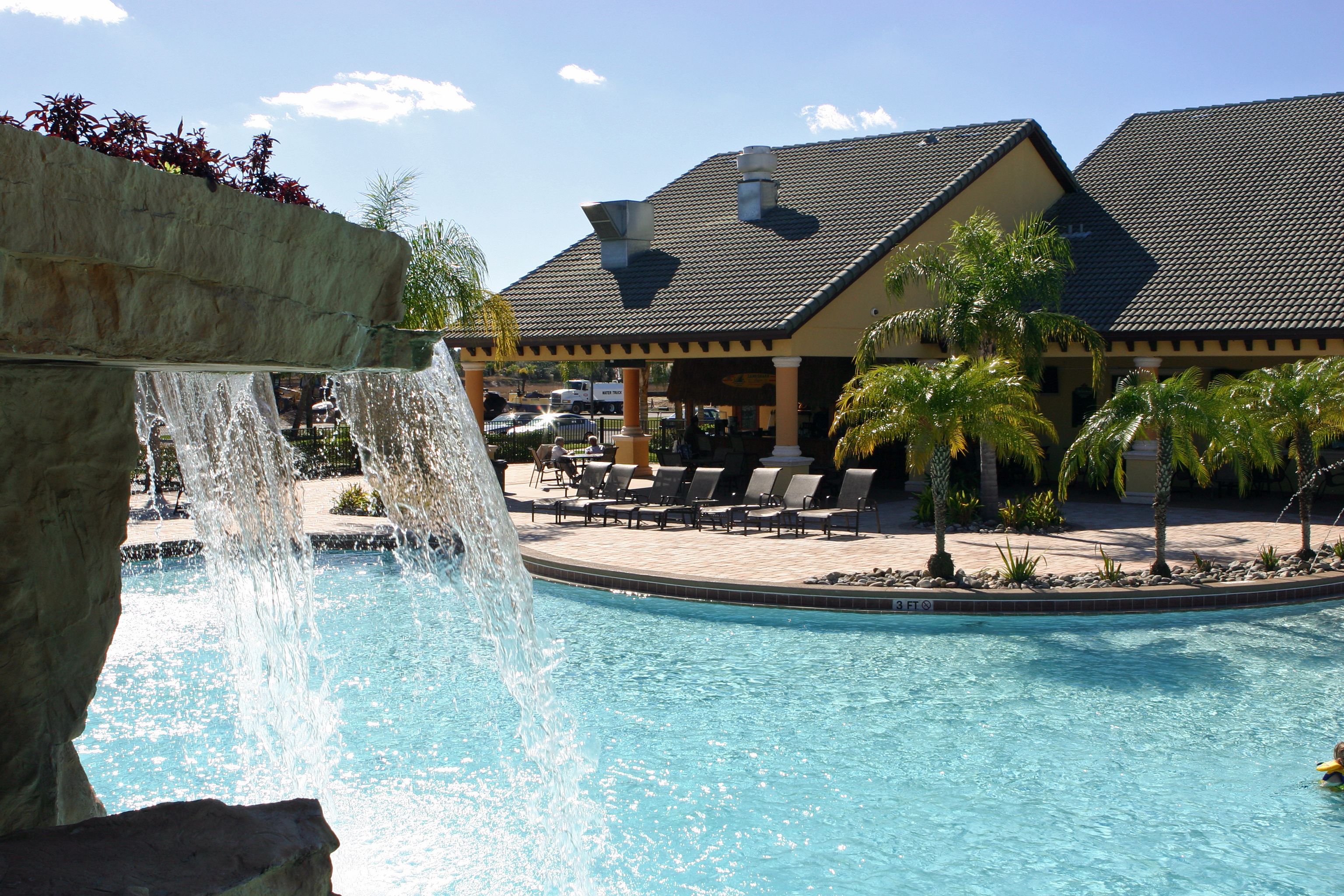 A pool with a waterfall feature, lounge chairs, and a building with a tiled roof in the background.