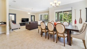 A spacious living room with a dining area, a flat-screen TV, and a large window offering a view of greenery. - Paradise Palms Resort Orlando (Kissimmee)