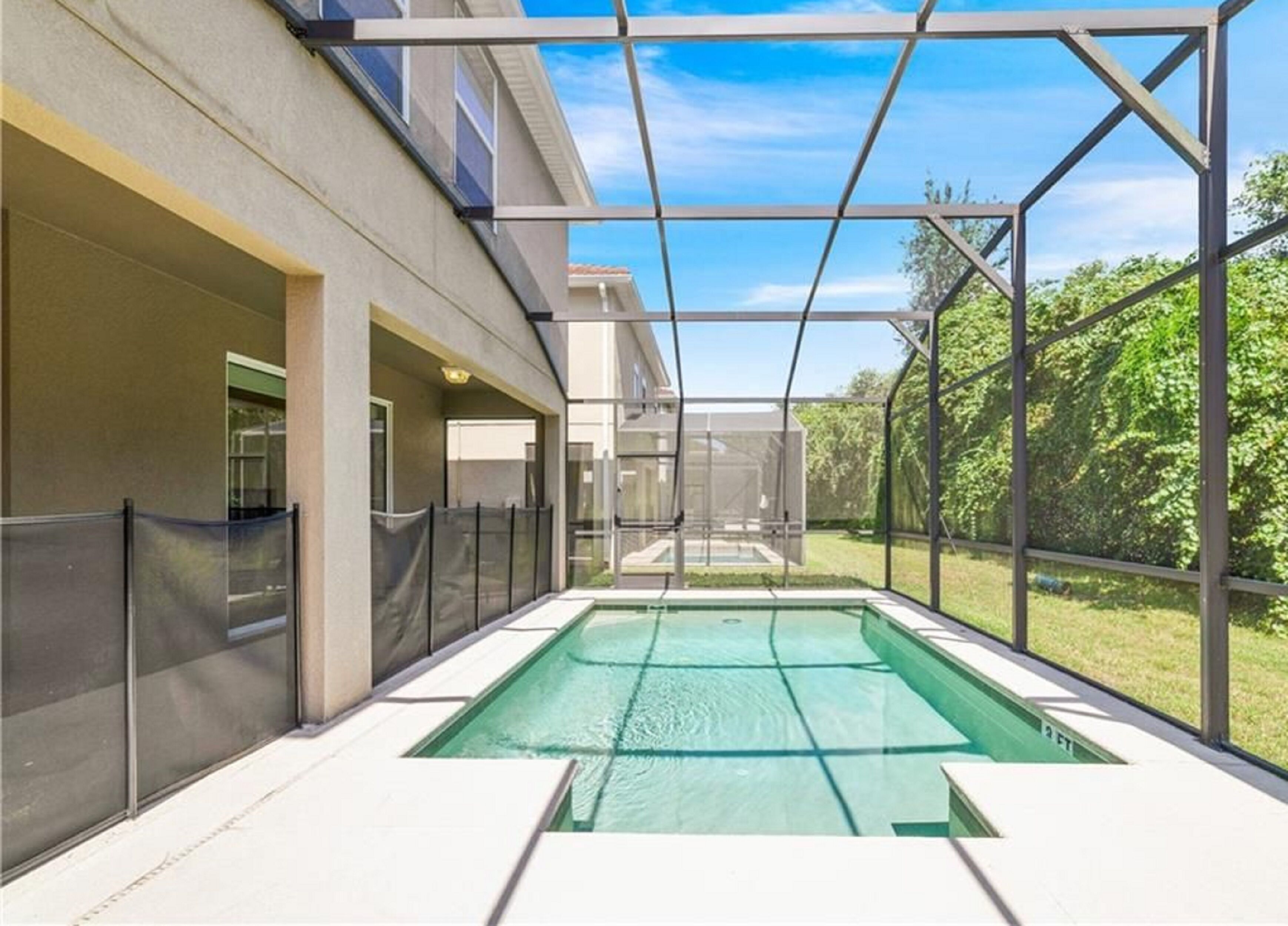 A modern indoor swimming pool with a glass enclosure, surrounded by a building with a concrete exterior and a view of greenery.