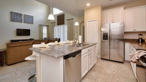 A modern kitchen with a central island, stainless steel appliances, and a dining area with a brown sofa. - Paradise Palms Resort Orlando (Kissimmee)