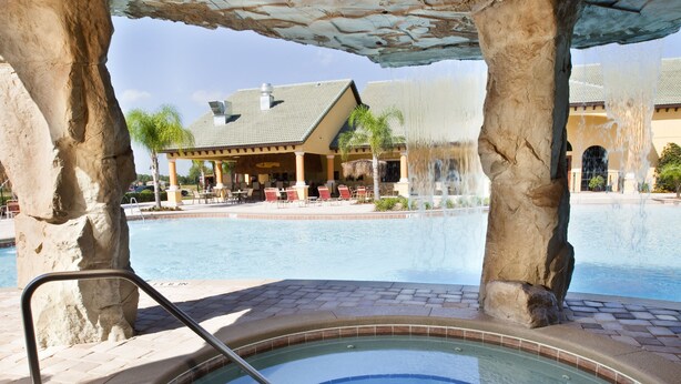 A hot tub under a stone structure with a pool and a building in the background. - Paradise Palms Resort Orlando (Kissimmee)